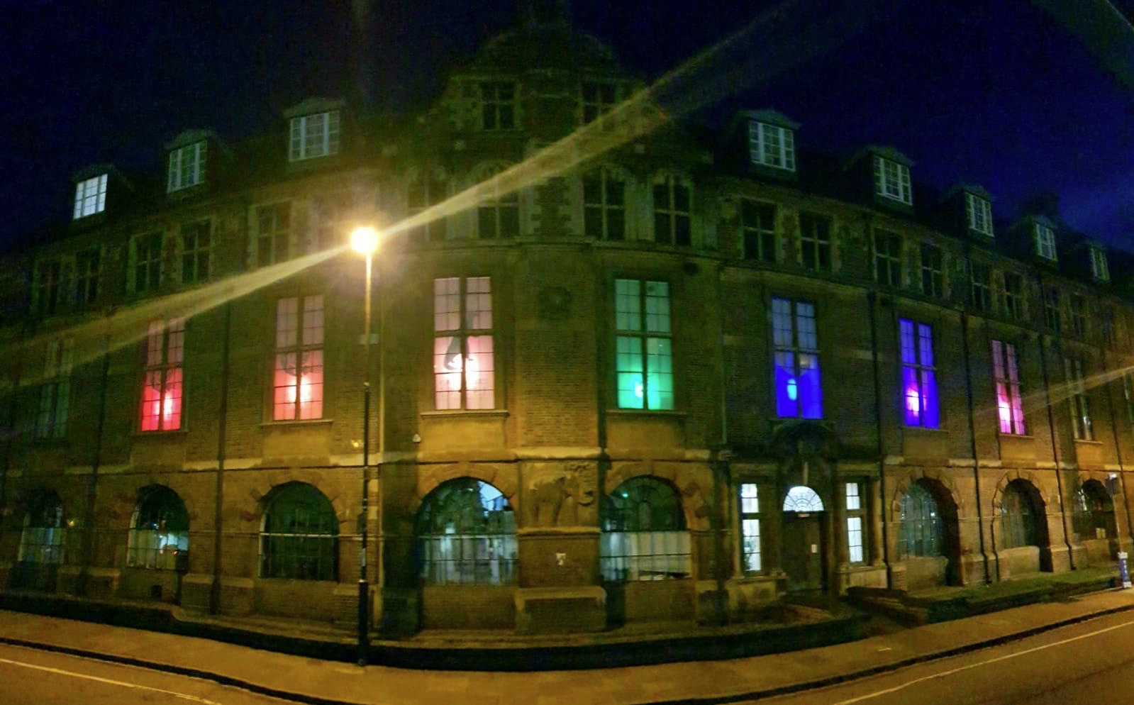 The windows of the museum are lit up in different colours, in the evening. Together the colours make a rainbow.