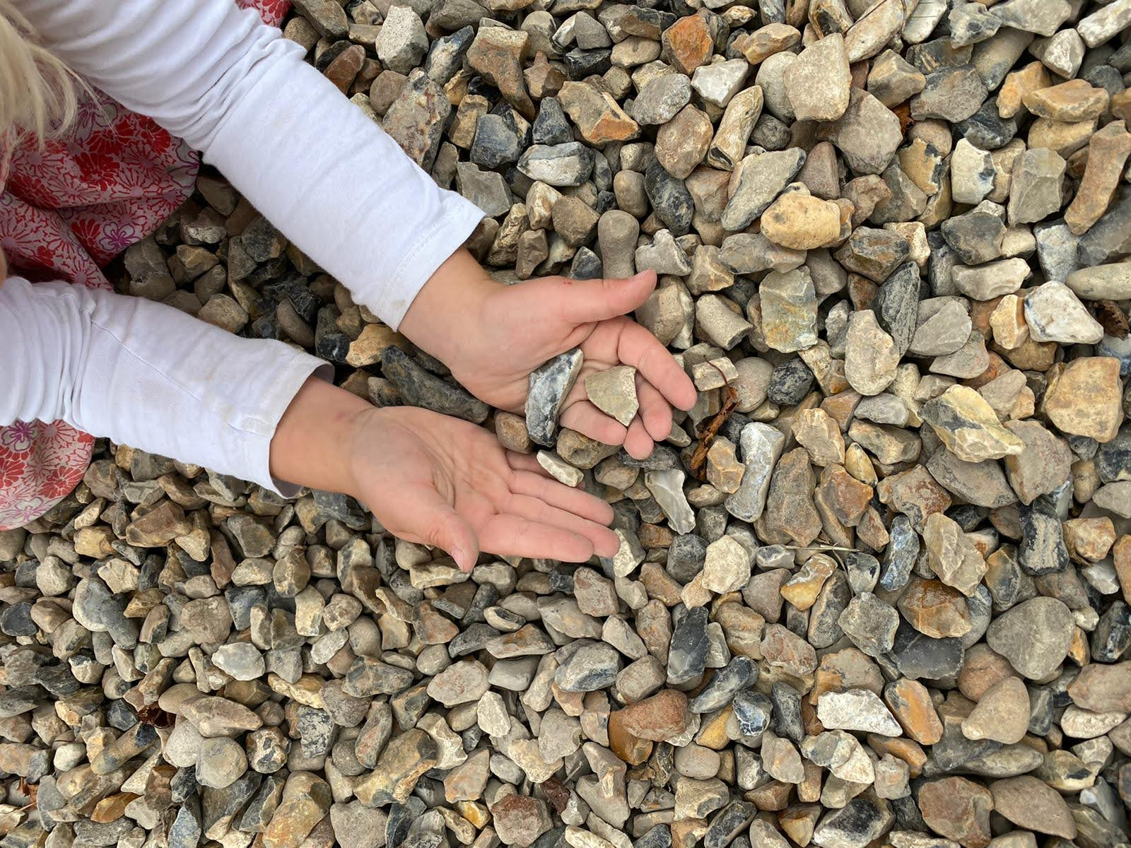 A child's hands are held above a floor of gravel, holding a few pieces of gravel.