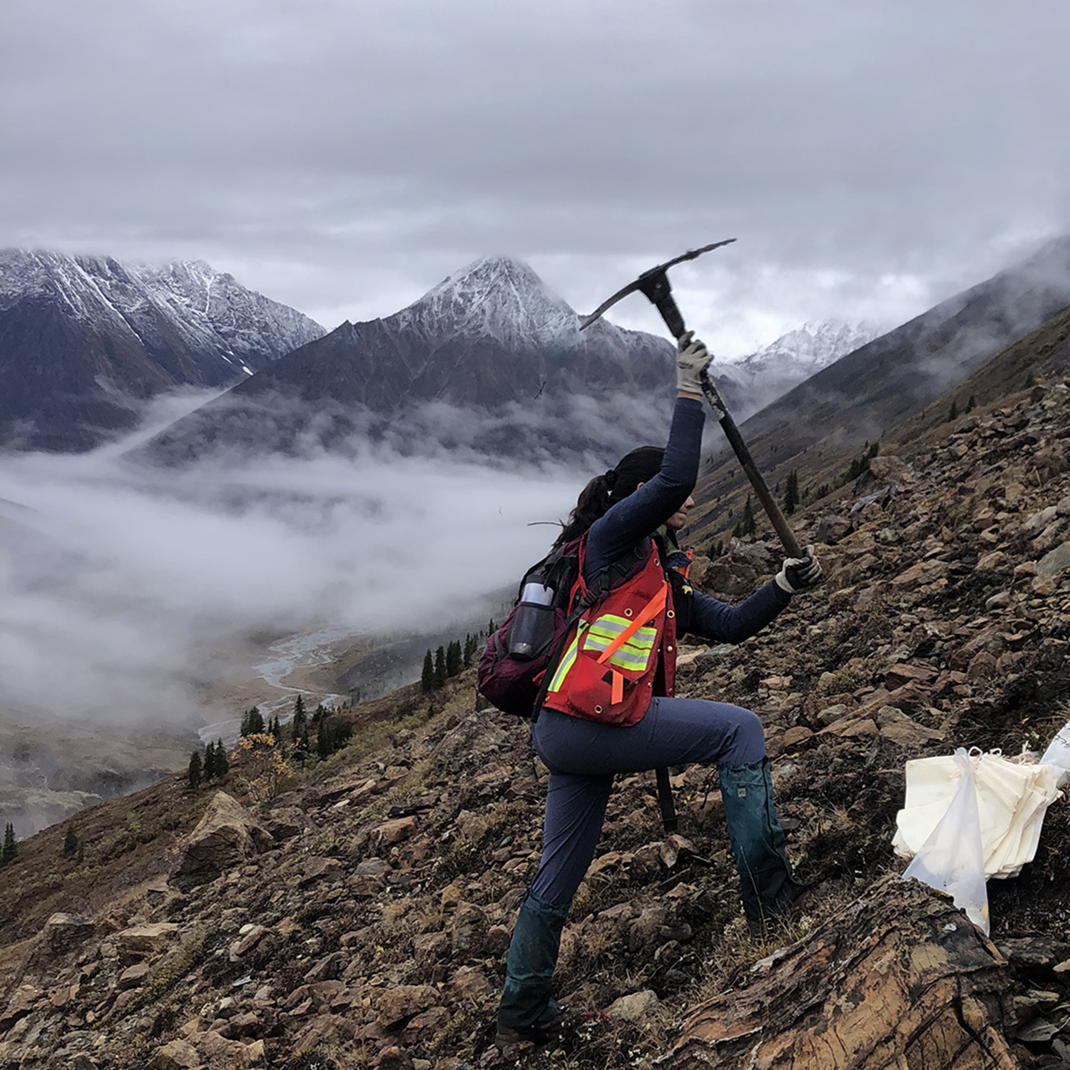 Earth scientist Ayesha weilds a geological hammer on a rocky slope in Canada.