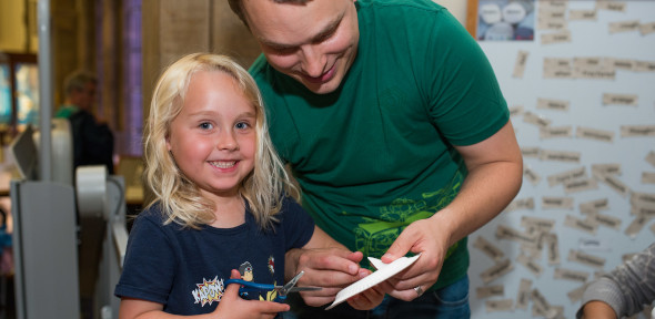 child holding scissors being helped by an adult to cut card