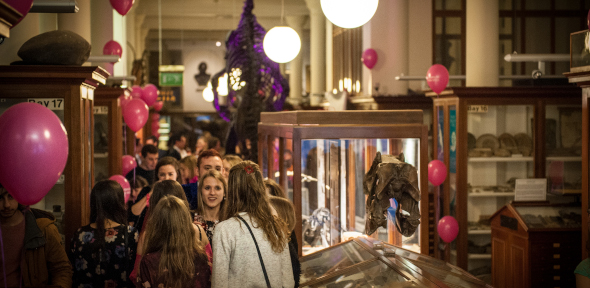 group of students celebrating in the museum gallery with reduced lighting and pink balloons